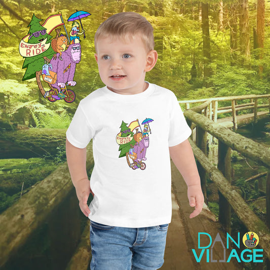 Funny illustrated toddler tee featuring a bigfoot happily riding a bike